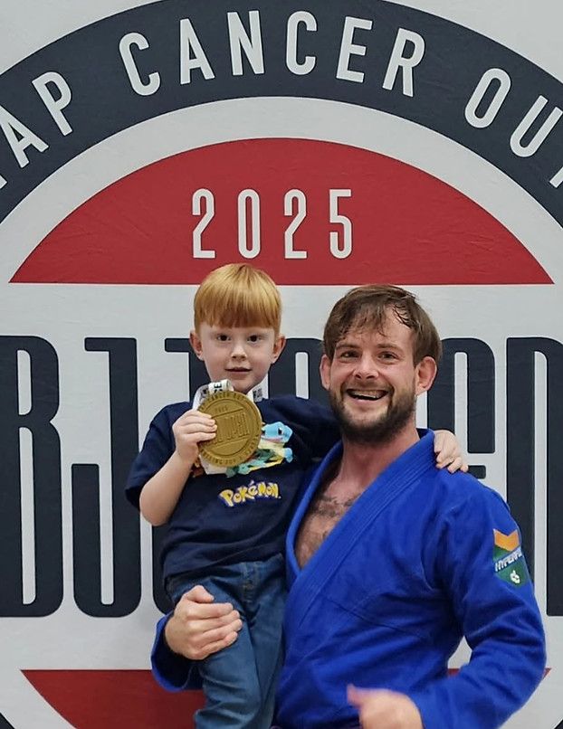 Coach Eric Decker with a young supporter holding a medal at Tap Cancer Out 2025